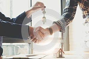 Estate agent shaking hands with his customer after contract signature, Contract document and house model on wooden desk