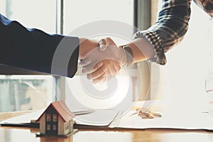 Estate agent shaking hands with his customer after contract signature, Contract document and house model on wooden desk