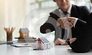 Estate agent shaking hands with his customer after contract signature, Contract document and house model on wooden desk