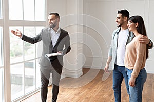 Estate Agent In Suit Showing Buyers New Empty Apartment