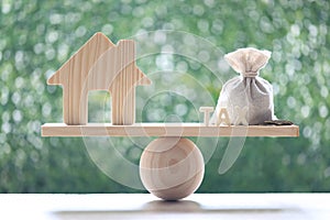 Estate tax,Model house with money bag and tax word on seesaw green background,Business investment and Property tax concept