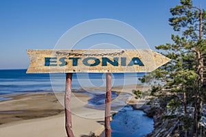 Estonia wooden arrow road sign against Baltic sea beach and pine trees background. Travel to Estonia concept