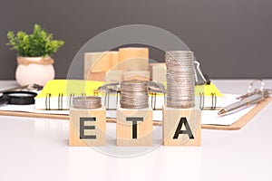 ETA text in wooden blocks with coins stacked in increasing stacks. Estimated Time Of Arrival concept