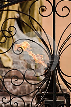 An eternal flame looking thru a wrought iron gate