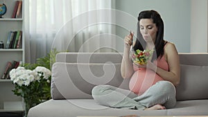 Eternally hungry pregnant girl eating salad, saturating body with vitamins