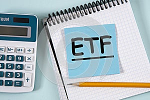 ETF - acronym in a white notebook on a blue piece of paper on the background of a calculator