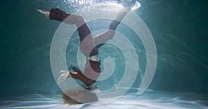 Ethereal cinematic background, young beautiful swimmer woman walks upside down under water, feet on surface slow motion