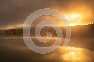 Ethereal moody sunrise with fog and steam being illuminated over a lake. Croton Gorge