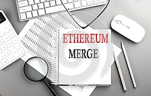 ETHEREUM MERGE text on notepad on chart with keyboard and calculator on grey background