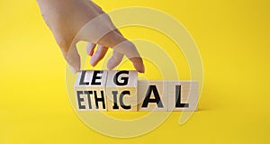 Ethical and Legal symbol. Businessman hand turnes wooden cubes and changes word Ethical to Legal. Beautiful yellow background.