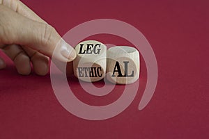 Ethical or legal symbol. Businessman turns wooden cubes and changes the word Ethical to Legal on a beautiful burgundy background.