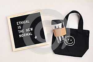 Ethical is the new normal letterboard text. Black organic cotton eco bag and reusable coffee cup. Zero waste sustainable