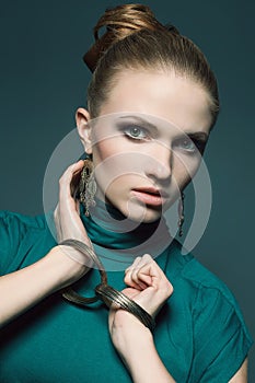 Ethnic accessories concept. Portrait of a beautiful young blonde in a green blue dress wearing golden earrings and wristbands