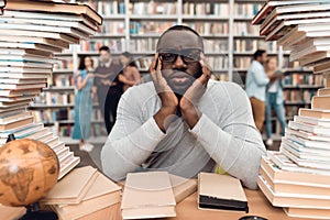 Ethnic african american guy surrounded by books in library. Student is bored and tired.