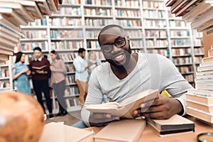 Ethnic african american guy surrounded by books in library. Student is reading book.