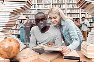 Ethnic african american guy and white girl surrounded by books in library. Students are reading book.