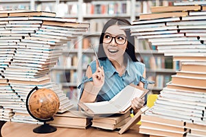 Ethnic asian girl sitting at table surrounded by books in library. Student is writing in notebook.