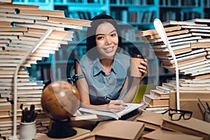 Ethnic asian girl surrounded by books in library. Student is writing in notebook.