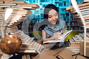 Ethnic asian girl surrounded by books in library. Student is writing in notebook.