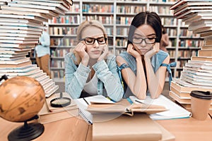 Ethnic asian girl and white girl surrounded by books in library. Students are reading book.
