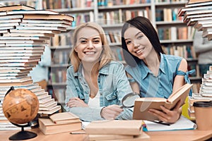 Ethnic asian girl and white girl surrounded by books in library. Students are reading book.