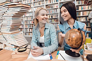 Ethnic asian girl and white girl surrounded by books in library. Students are using globe.