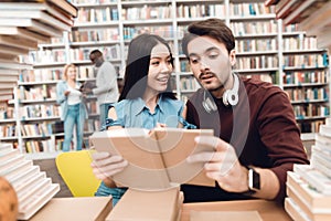 Ethnic asian girl and white guy surrounded by books in library. Students are reading book.