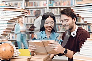 Ethnic asian girl and white guy surrounded by books in library. Students are reading book.