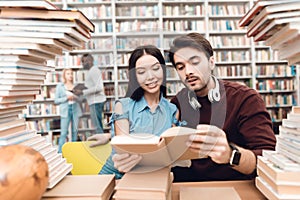 Ethnic asian girl and white guy surrounded by books in library. Students are reading book.