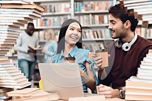 Ethnic asian girl and white guy surrounded by books in library. Students are using laptop.
