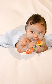 Ethnic baby boy with toy lying down on blanket