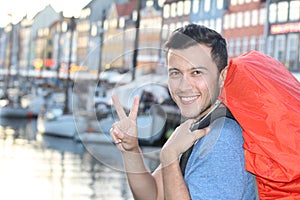 Ethnic backpacker smiling and showing a peace sign in the epic Nyhavn, Copenhagen, Denmark