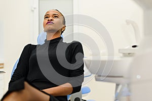 Ethnic black female patient sitting looking up on dental chair waiting for her dentist