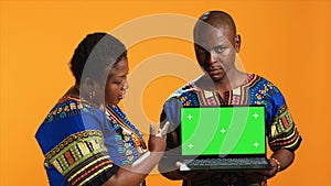 Ethnic couple pointing at laptop with greenscreen display