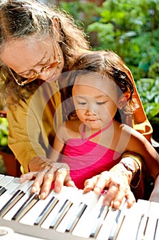 Ethnic elderly woman teach child play piano