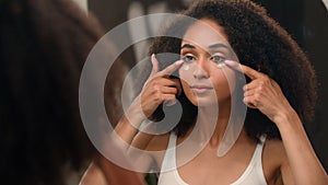 Ethnic girl beauty routine in morning young African American woman applying face cream under eyes anti-aging skin care