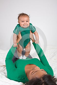 Ethnic mother playing with her baby boy son on bed