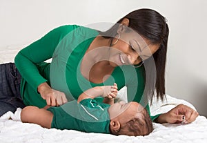 Ethnic mother playing with her baby boy son on bed