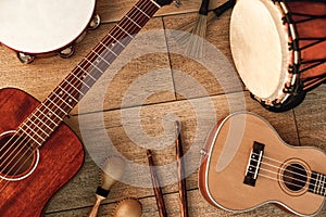 Ethnic musical instruments set: tambourine, wooden drum, brushes, wooden sticks, maracas and guitars laying on wooden