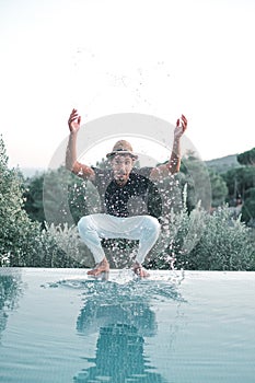 Ethnic Stylish young man splashing water near a swimming pool