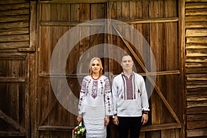 Ethnic wedding in national costumes. Ukrainian marriage bride and groom standing on the background of a wooden wall