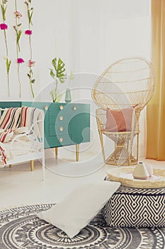 Ethno carpet on white floor of stylish bedroom interior with green furniture and wicker peacock chair