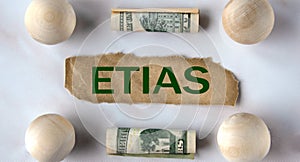 ETIAS - word on a brown torn piece of paper on the background of light balls and banknotes