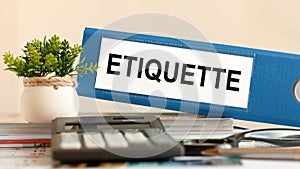 ETIQUETTE - blue binder on desk in the office with calculator, pen and green potted plant, concept photo