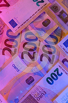 EU currency. Two hundred euro bills close-up in purple neon light. Money colored background.Inflation of money in the EU