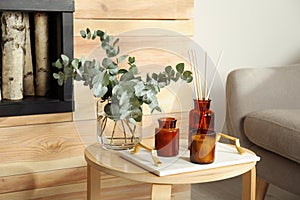 Eucalyptus branches, aromatic reed air freshener and candles on wooden table in living room. Interior element