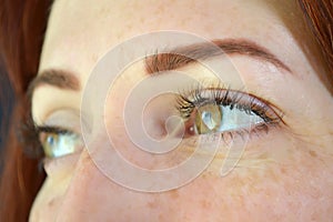 Eues of girl with red hair and green eyes with freckles with eyelash extensions on a dark background looks right