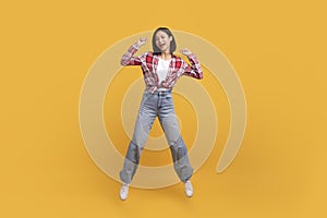 Euphoria concept. Full length shot of asian lady jumping and clenching fists isolated on yellow studio background