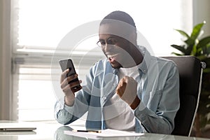 Euphoric millennial african american businessman looking at mobile phone screen.