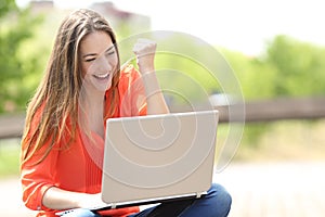 Euphoric woman searching job with a laptop in a park photo